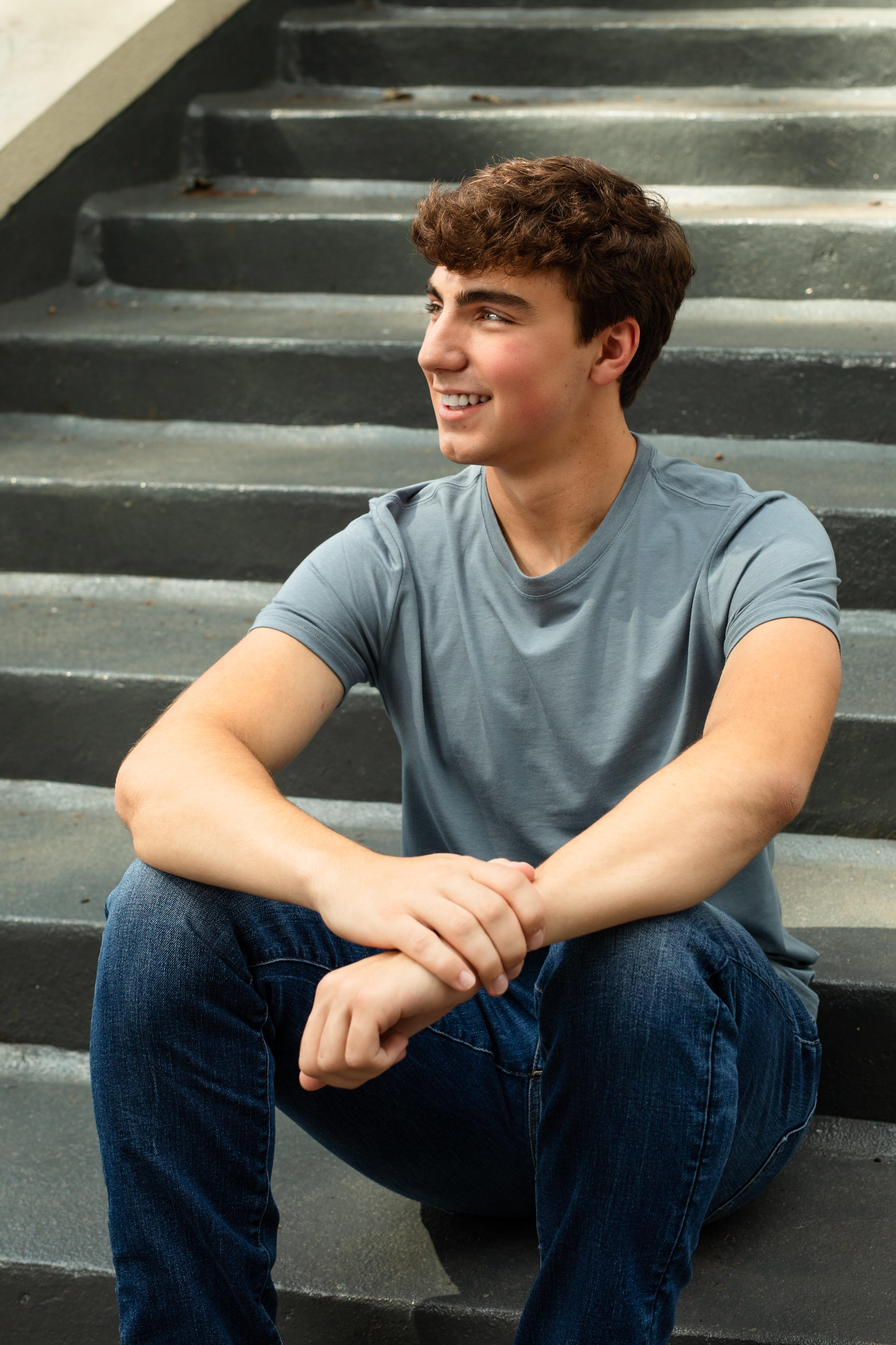 Jacob Tartabini sitting on outdoor steps in a blue tee, looking off-camera