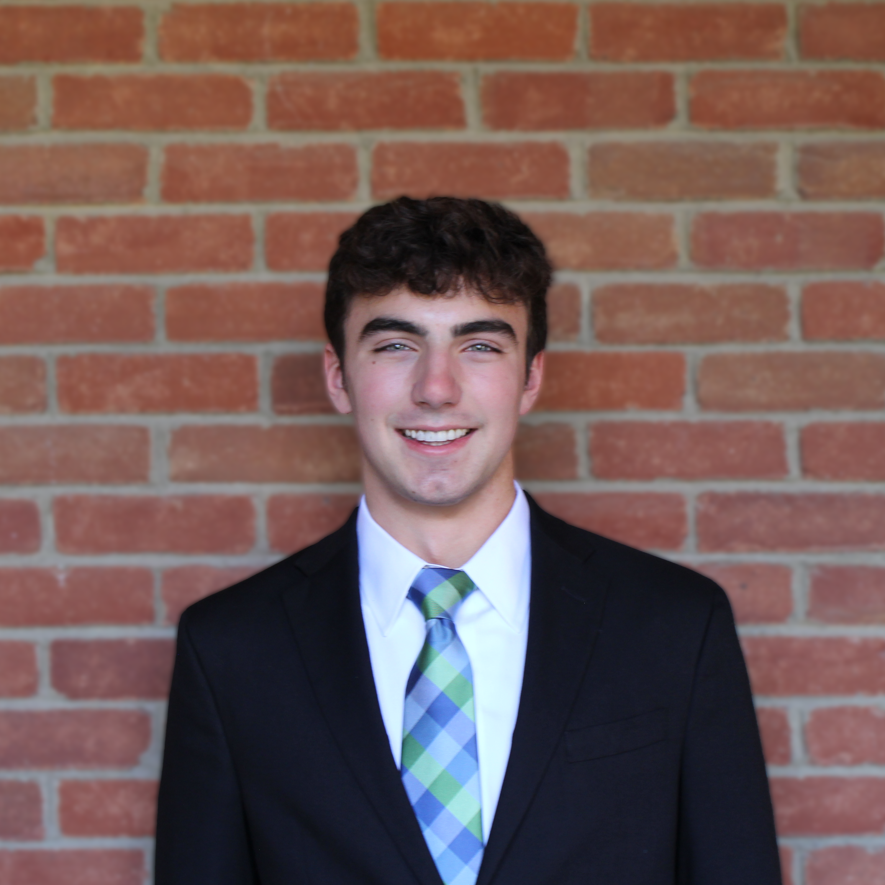 Jacob Tartabini in a dark suit and plaid tie in front of a brick wall